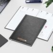 Wochenkalender als Werbegeschenk 2026: Schwarzer Einband, Kupferprägung, Kalender mit Logo auf Schreibtisch.