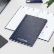 Wochenkalender mit eigenem Logo für 2026: Blauer Einband mit Silberprägung, Kalender mit Logo auf dem Schreibtisch.
